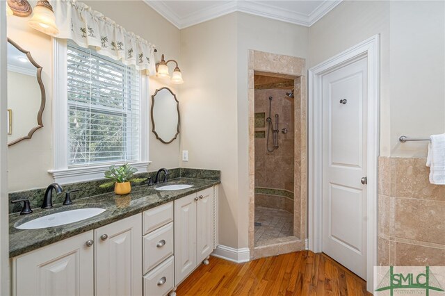 bathroom with a sink, wood finished floors, crown molding, and a tile shower