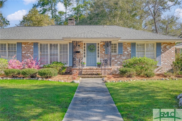 ranch-style house featuring brick siding, a chimney, a front lawn, and roof with shingles