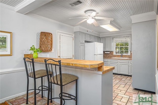 kitchen featuring crown molding, decorative backsplash, a peninsula, a kitchen breakfast bar, and freestanding refrigerator