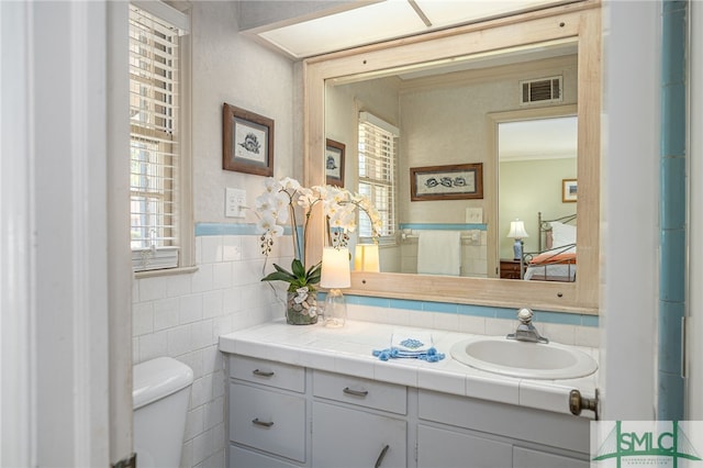 half bathroom with visible vents, toilet, ornamental molding, tile walls, and vanity