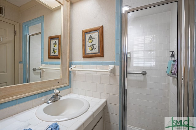 bathroom featuring visible vents, a wainscoted wall, vanity, a stall shower, and tile walls