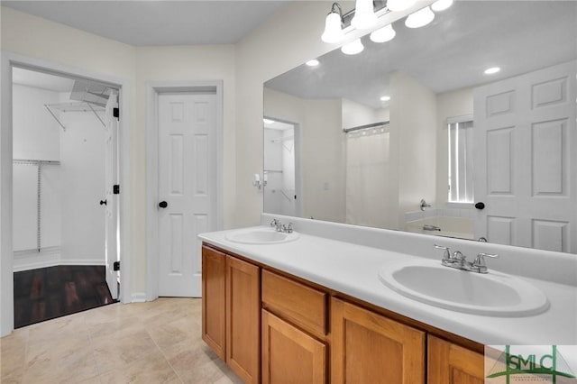 bathroom with double vanity, a tub, a walk in closet, and a sink