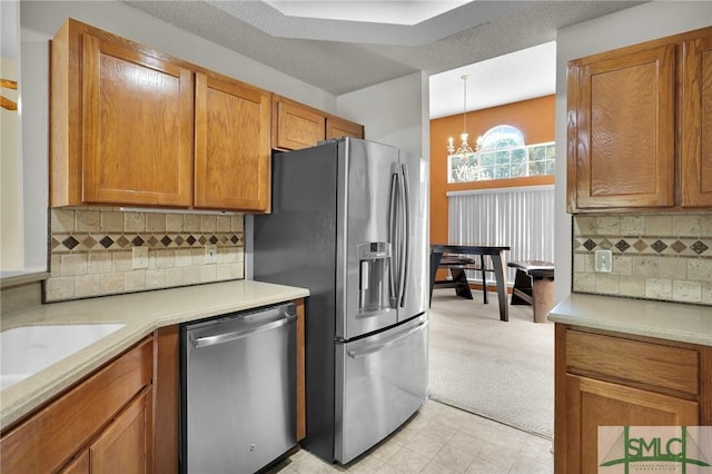 kitchen featuring stainless steel appliances, light countertops, light carpet, a notable chandelier, and brown cabinets