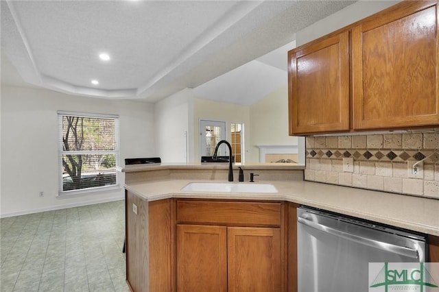 kitchen featuring dishwasher, light countertops, a tray ceiling, a peninsula, and a sink