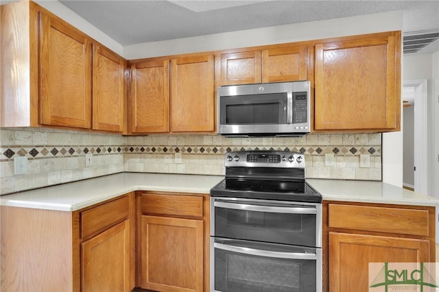 kitchen with tasteful backsplash, visible vents, light countertops, brown cabinets, and stainless steel appliances