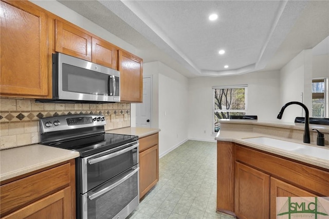 kitchen featuring brown cabinetry, light floors, a sink, appliances with stainless steel finishes, and a raised ceiling