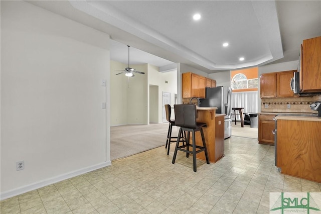 kitchen with a breakfast bar, decorative backsplash, appliances with stainless steel finishes, a raised ceiling, and a ceiling fan