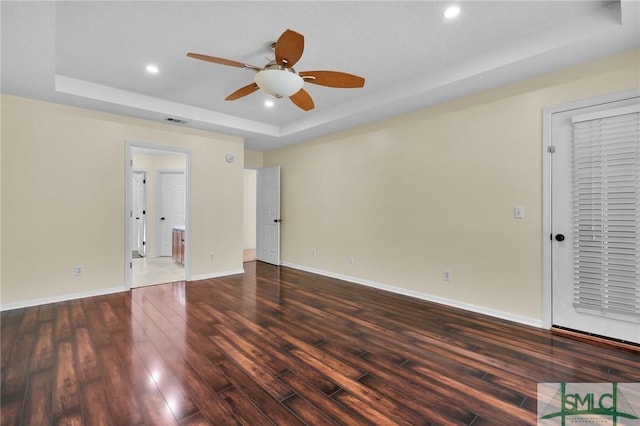 empty room with ceiling fan, visible vents, a raised ceiling, and wood finished floors