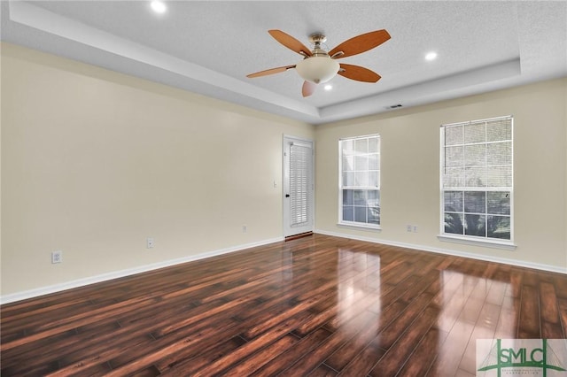 spare room with a raised ceiling, baseboards, dark wood-type flooring, and ceiling fan