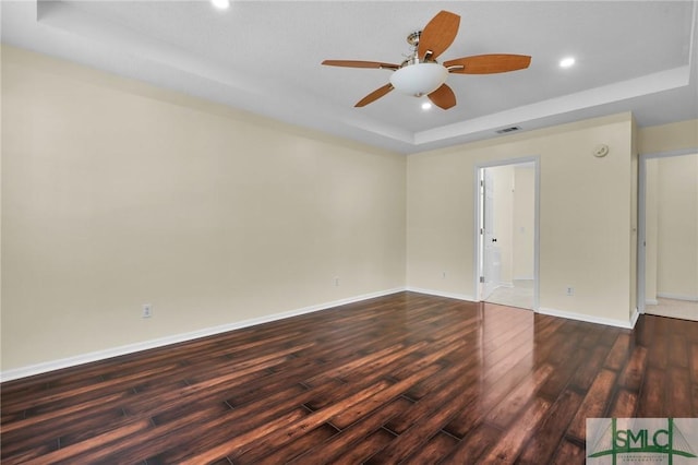 spare room with visible vents, a ceiling fan, baseboards, a raised ceiling, and dark wood-style flooring