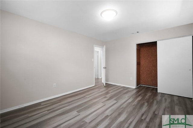 unfurnished bedroom with a closet, visible vents, baseboards, and wood finished floors