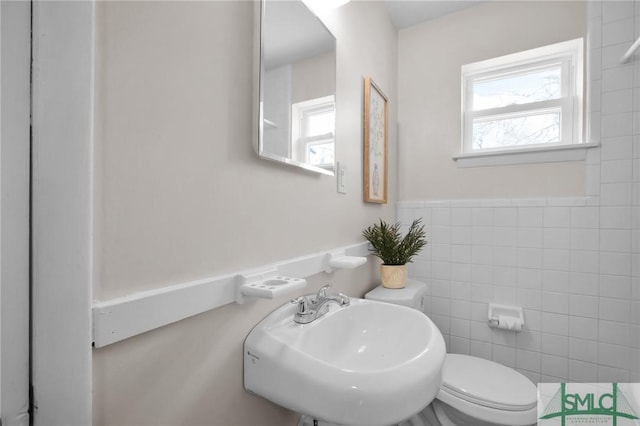 bathroom featuring tile walls, toilet, and a sink