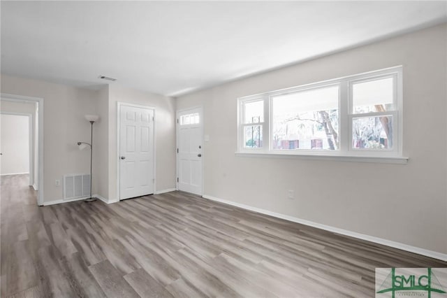 unfurnished living room featuring visible vents, baseboards, and wood finished floors