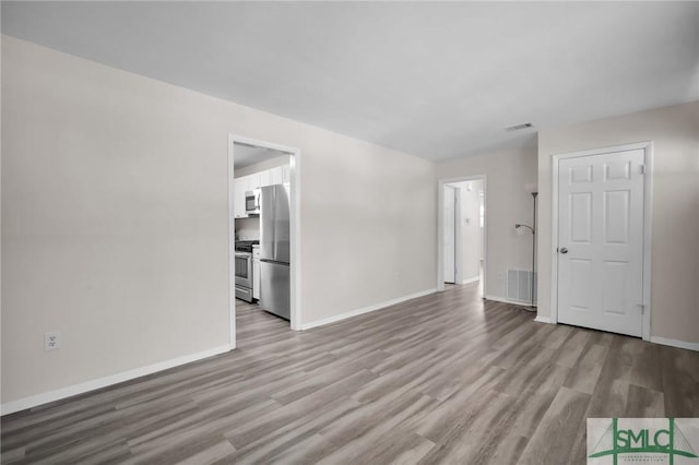 unfurnished living room featuring visible vents, baseboards, and wood finished floors