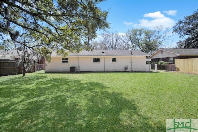 rear view of house with central air condition unit, a lawn, a fenced backyard, and stucco siding