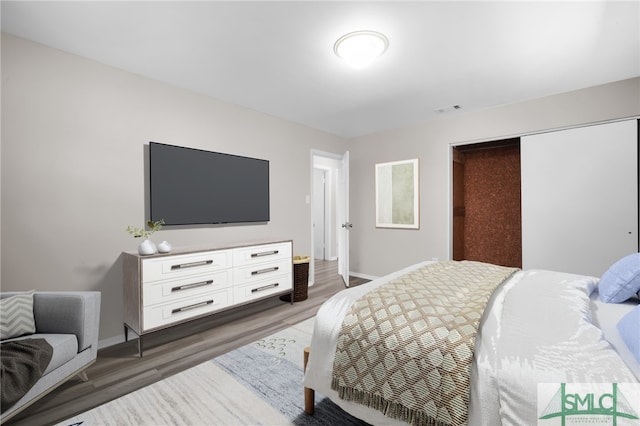 bedroom with a closet, visible vents, baseboards, and wood finished floors