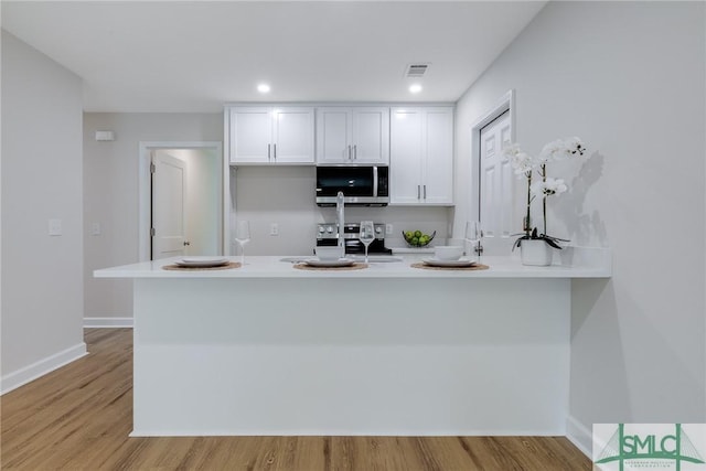 kitchen with visible vents, a peninsula, stainless steel appliances, white cabinets, and light wood-style floors