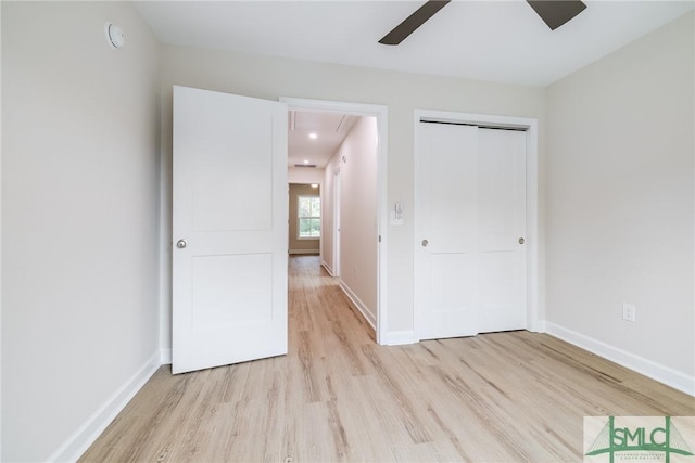 unfurnished bedroom featuring baseboards, attic access, light wood-style flooring, ceiling fan, and a closet