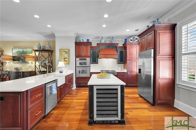 kitchen featuring reddish brown cabinets, premium range hood, wine cooler, stainless steel appliances, and a sink