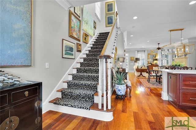 staircase featuring recessed lighting, wood finished floors, baseboards, and ornamental molding