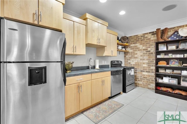 kitchen featuring a sink, brick wall, light brown cabinetry, and stainless steel appliances