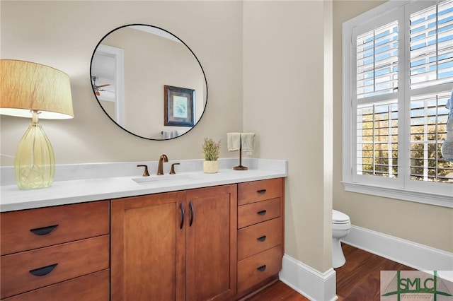 half bath featuring toilet, vanity, baseboards, and wood finished floors