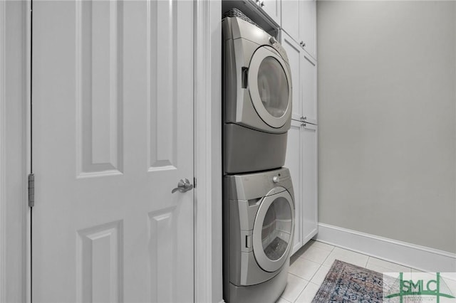 laundry area featuring stacked washer / dryer, light tile patterned floors, cabinet space, and baseboards