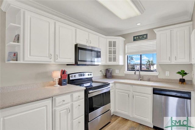 kitchen featuring white cabinets, appliances with stainless steel finishes, crown molding, and a sink