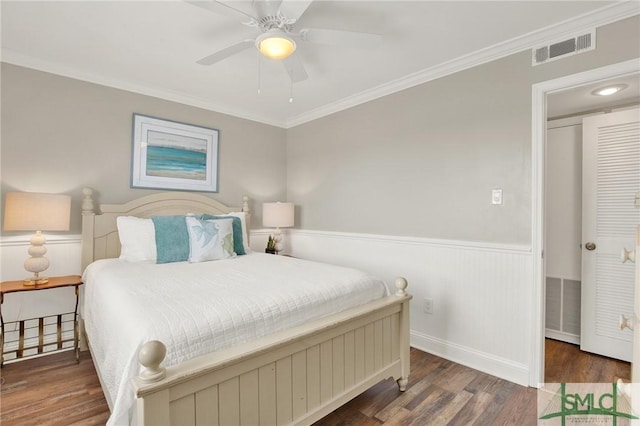 bedroom with a wainscoted wall, crown molding, wood finished floors, and visible vents