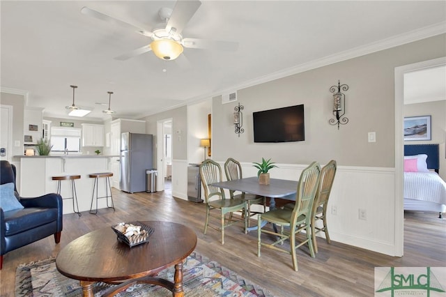 living area featuring visible vents, a wainscoted wall, dark wood finished floors, crown molding, and ceiling fan