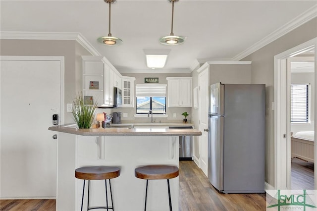 kitchen featuring wood finished floors, white cabinetry, a peninsula, appliances with stainless steel finishes, and a kitchen bar