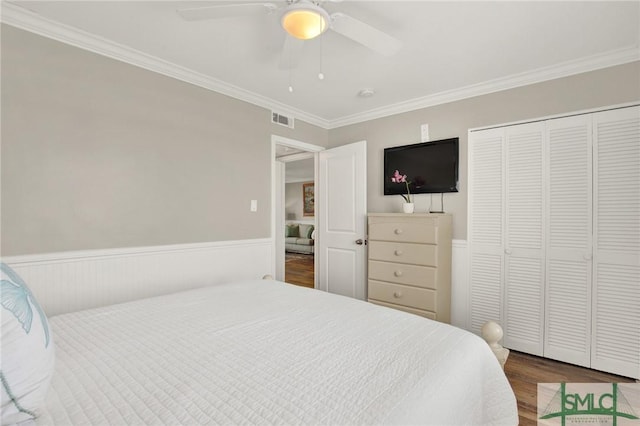 bedroom with wood finished floors, a wainscoted wall, visible vents, ornamental molding, and a closet