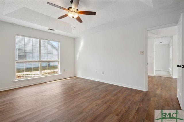 spare room featuring visible vents, dark wood-type flooring, a ceiling fan, a tray ceiling, and baseboards