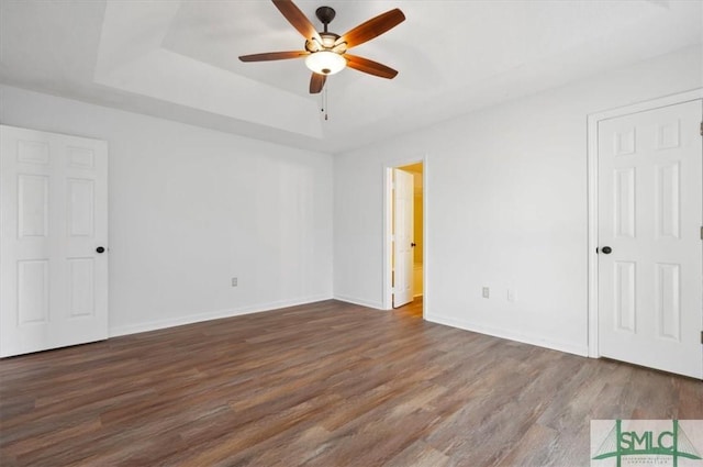 unfurnished bedroom with a tray ceiling, wood finished floors, and baseboards