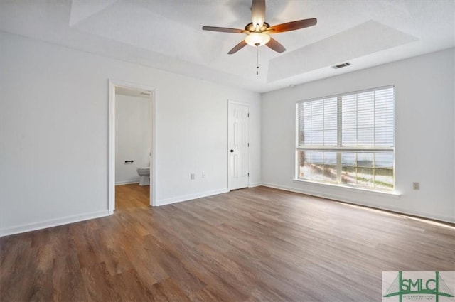 unfurnished bedroom with visible vents, a raised ceiling, baseboards, and wood finished floors