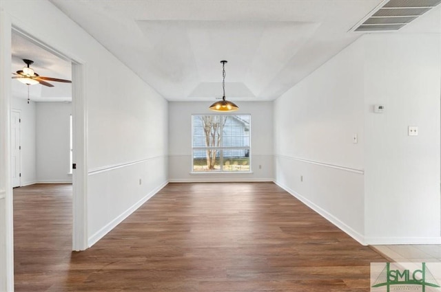 unfurnished dining area with a raised ceiling, wood finished floors, visible vents, and baseboards