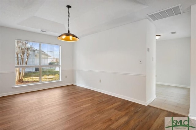 unfurnished room with a tray ceiling, visible vents, baseboards, and wood finished floors