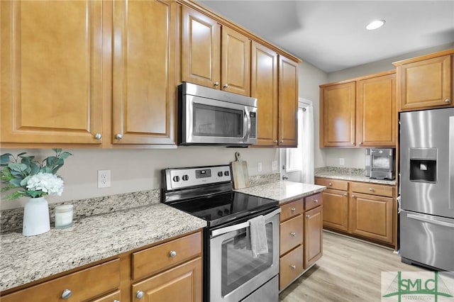 kitchen with light wood finished floors, light stone counters, recessed lighting, brown cabinetry, and stainless steel appliances