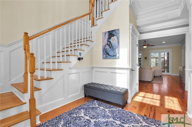 stairs with ornamental molding, wainscoting, wood finished floors, a decorative wall, and a ceiling fan