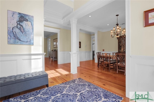 interior space featuring an inviting chandelier, light wood-style flooring, decorative columns, and crown molding