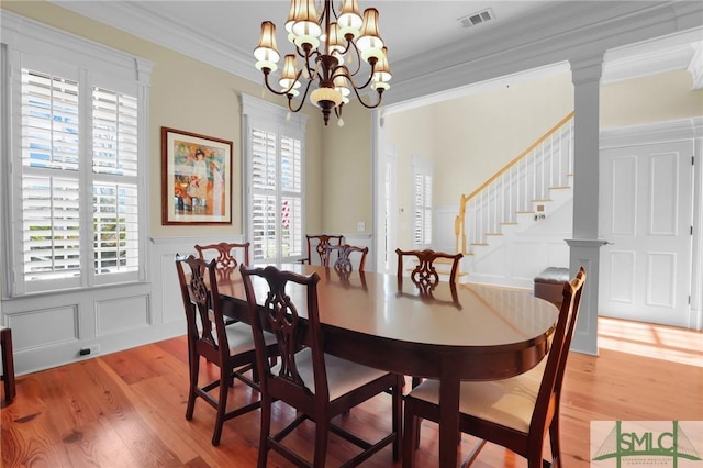 dining space featuring visible vents, ornamental molding, an inviting chandelier, light wood-style floors, and a decorative wall