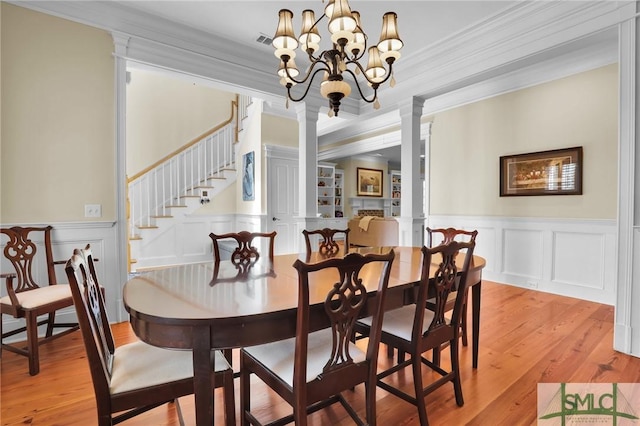 dining space with decorative columns, an inviting chandelier, light wood-style flooring, and crown molding