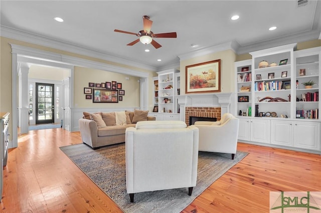 living room featuring light wood finished floors, a brick fireplace, crown molding, and a ceiling fan