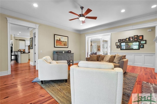 living area with ornamental molding, a ceiling fan, wood finished floors, recessed lighting, and a decorative wall