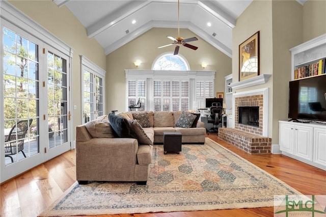 living area featuring light wood-type flooring, beam ceiling, high vaulted ceiling, a brick fireplace, and ceiling fan