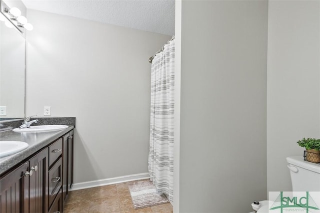 bathroom featuring baseboards, toilet, double vanity, a textured ceiling, and a sink