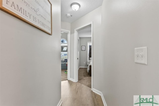 corridor featuring wood finished floors, baseboards, and a textured ceiling