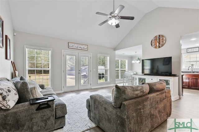 living area featuring ceiling fan with notable chandelier, wood finished floors, baseboards, and high vaulted ceiling