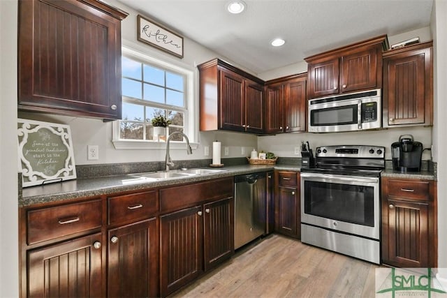 kitchen featuring light wood-style flooring, a sink, dark countertops, recessed lighting, and appliances with stainless steel finishes