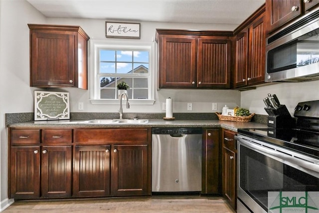 kitchen featuring light wood-style flooring, a sink, stainless steel appliances, dark brown cabinets, and dark countertops